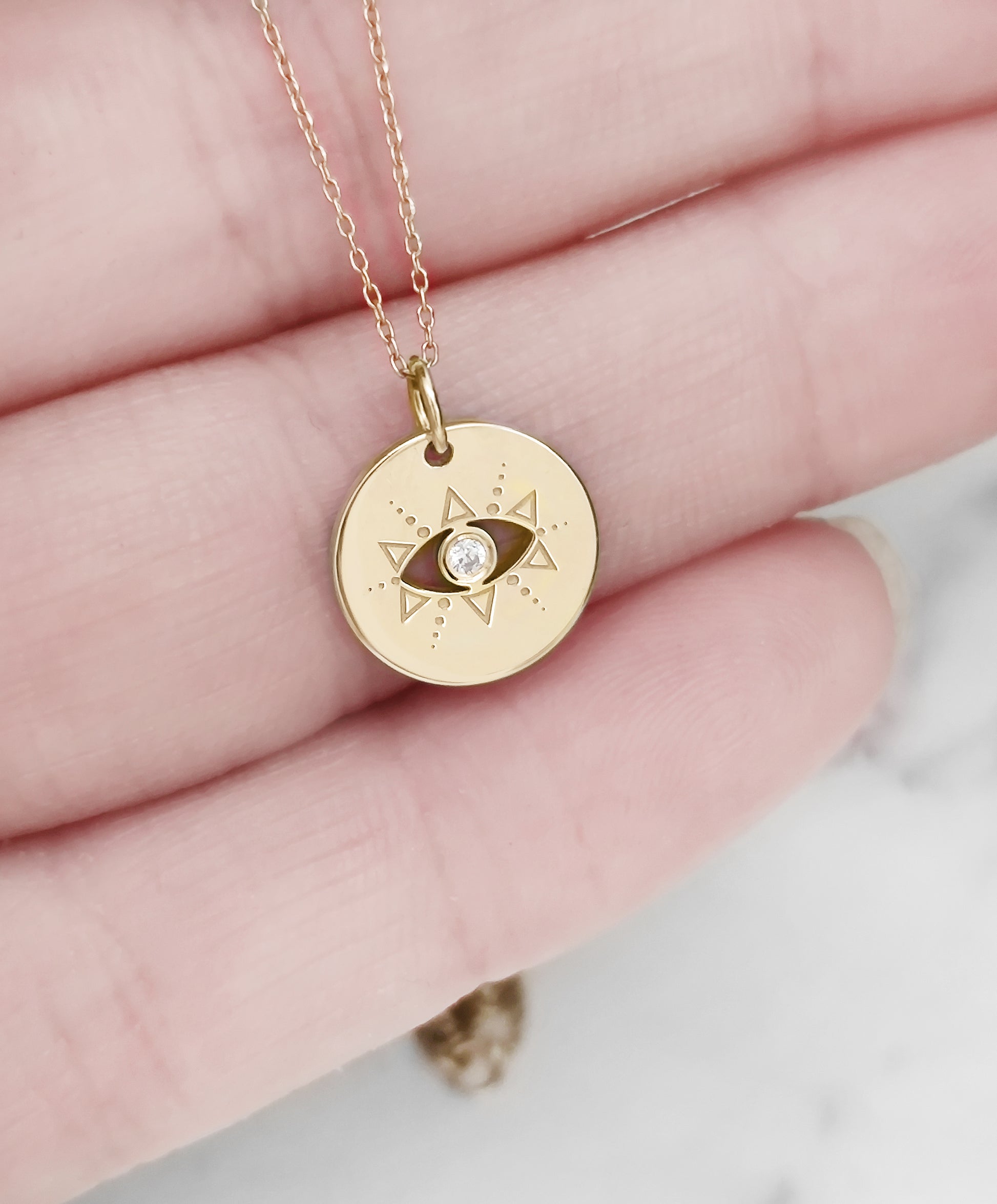 hand holding gold evil eye disc pendant necklace set with a diamond in the center for size reference