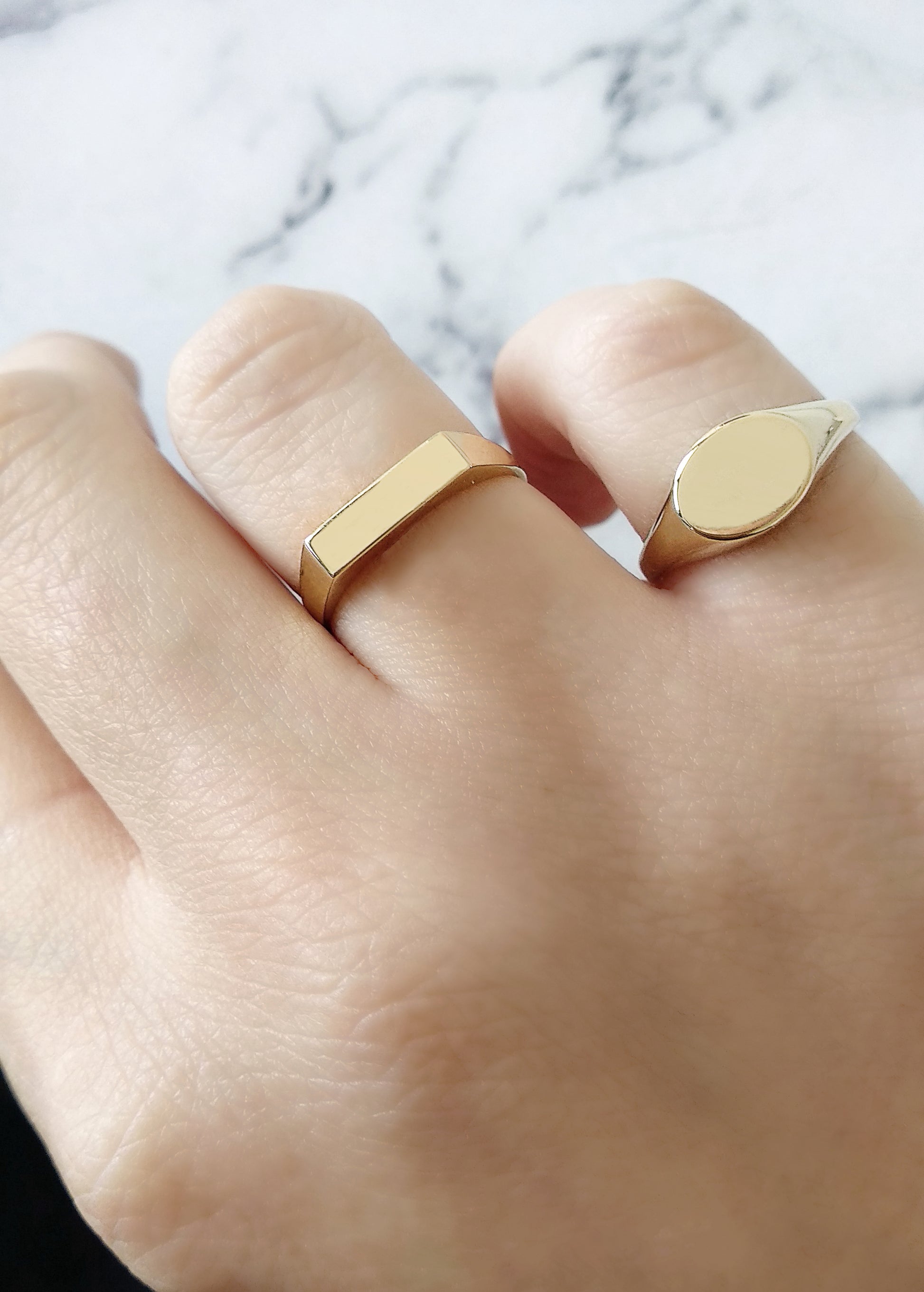 female hand wearing gold dainty oval signet ring on her pinky and thin bar ring on her ring finger