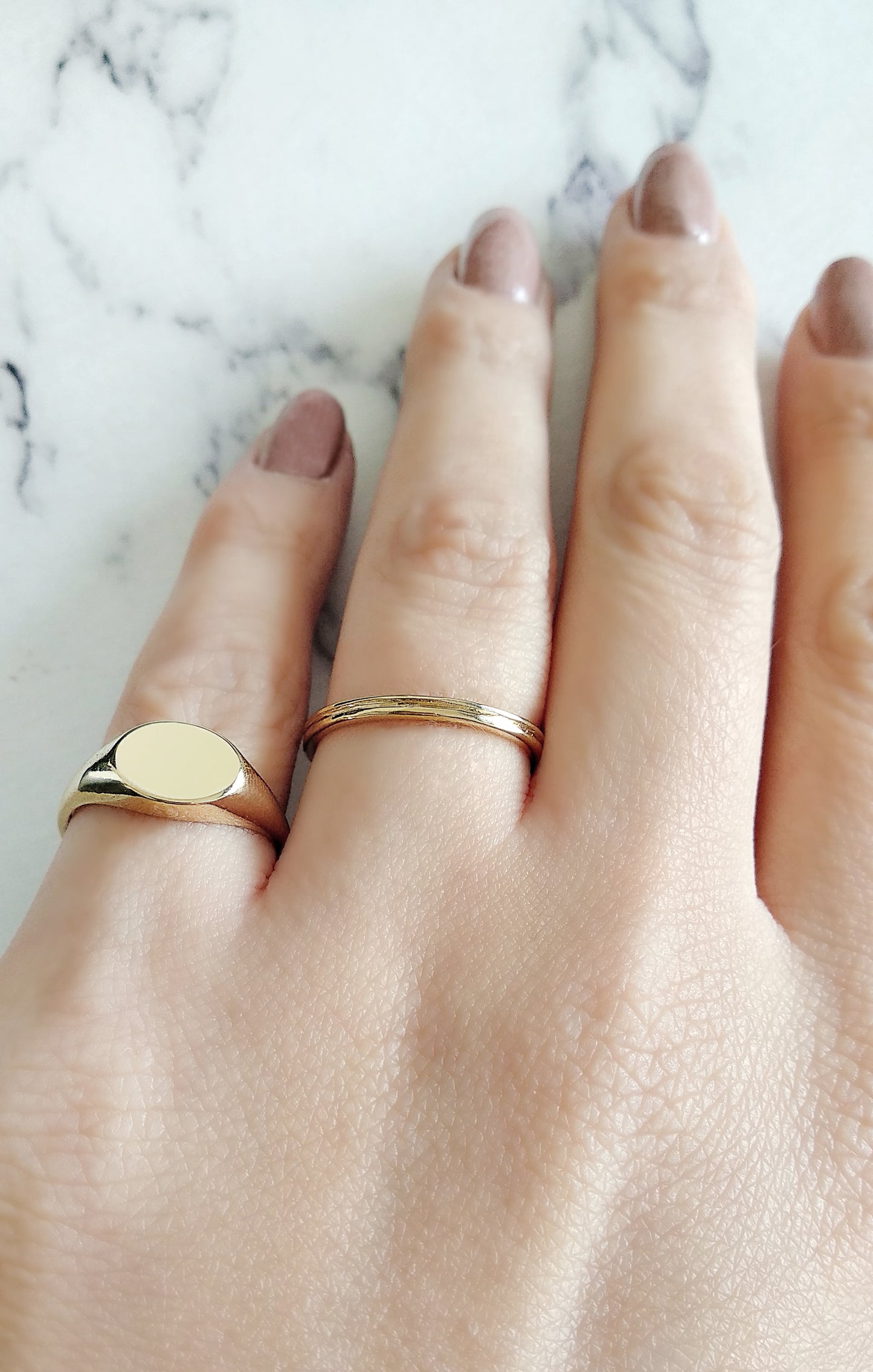 female hand wearing gold dainty oval signet ring on her pinky and a simple band in her ring finger