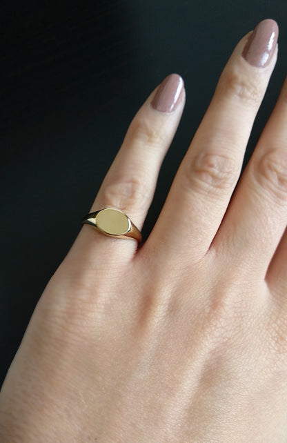 female hand wearing gold dainty oval signet ring on her pinky