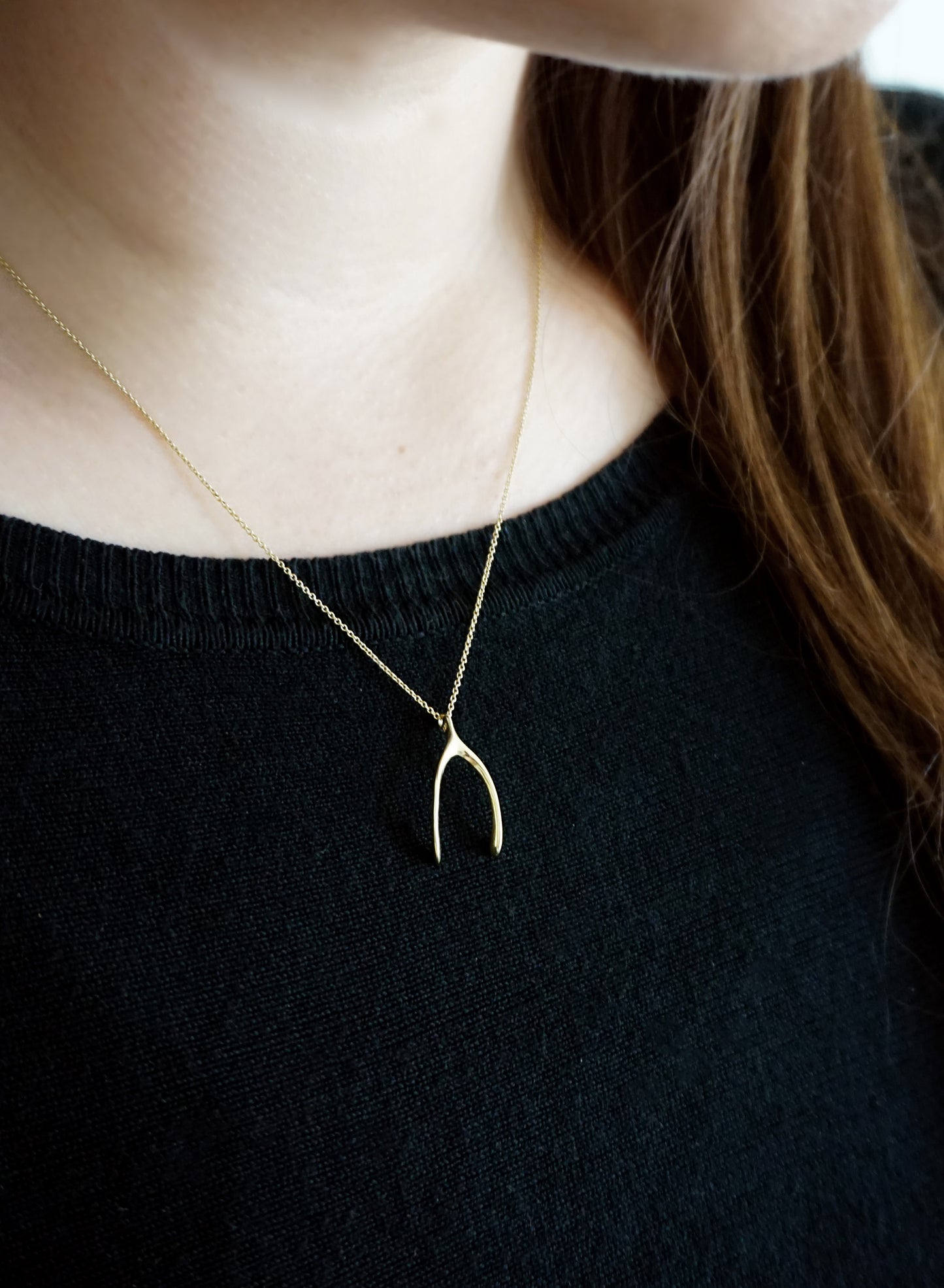 female wearing solid yellow gold wishbone pendant necklace