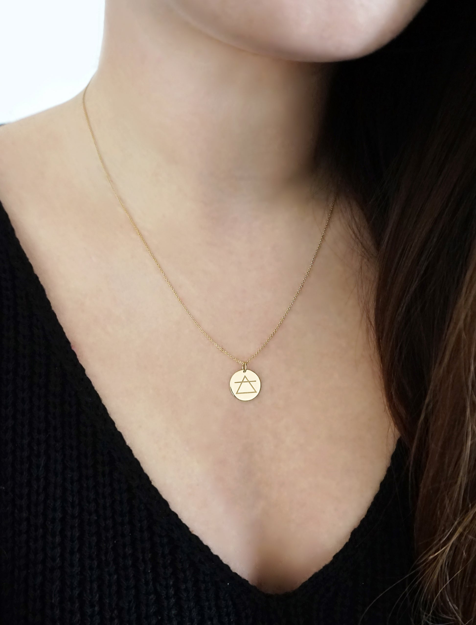 woman wearing a yellow gold necklace with a 14mm disc pendant engraved with the air element symbol