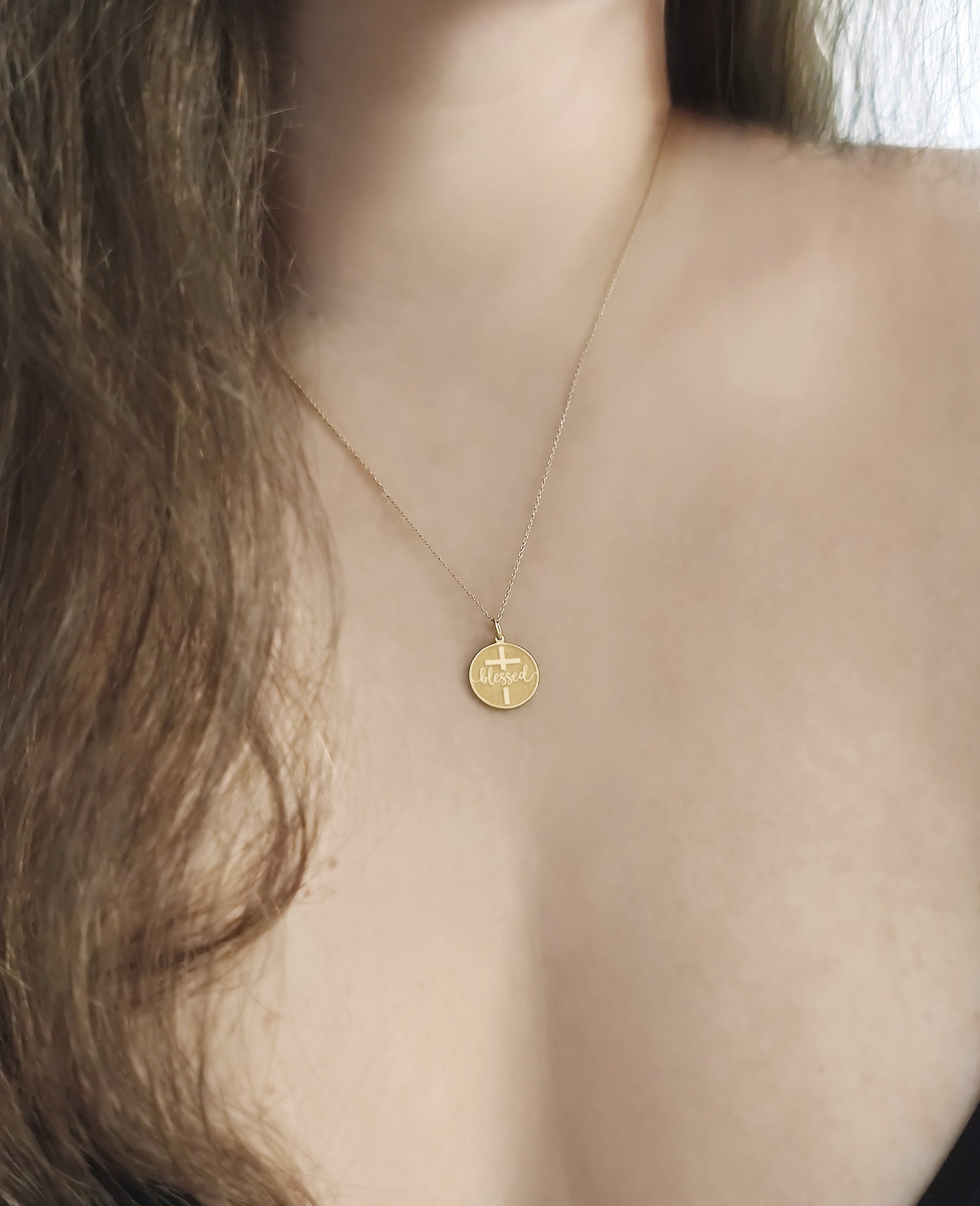 female wearing yellow gold necklace with a disc pendant engraved with the word blessed and a cross 