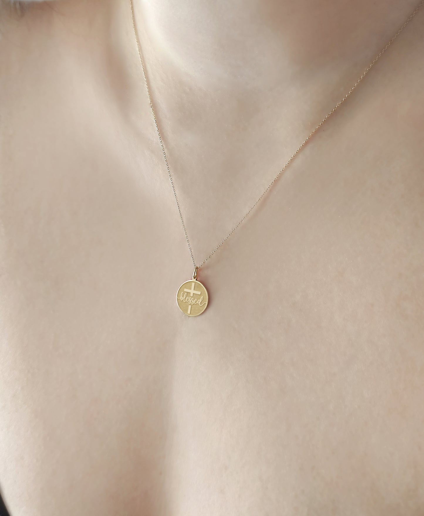 female wearing a gold necklace with a disc pendant engraved with the word blessed and a cross 