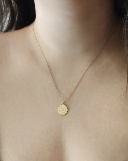 close up of a woman's neck wearing yellow gold disc pendant necklace engraved with a lion head and a circle frame around it