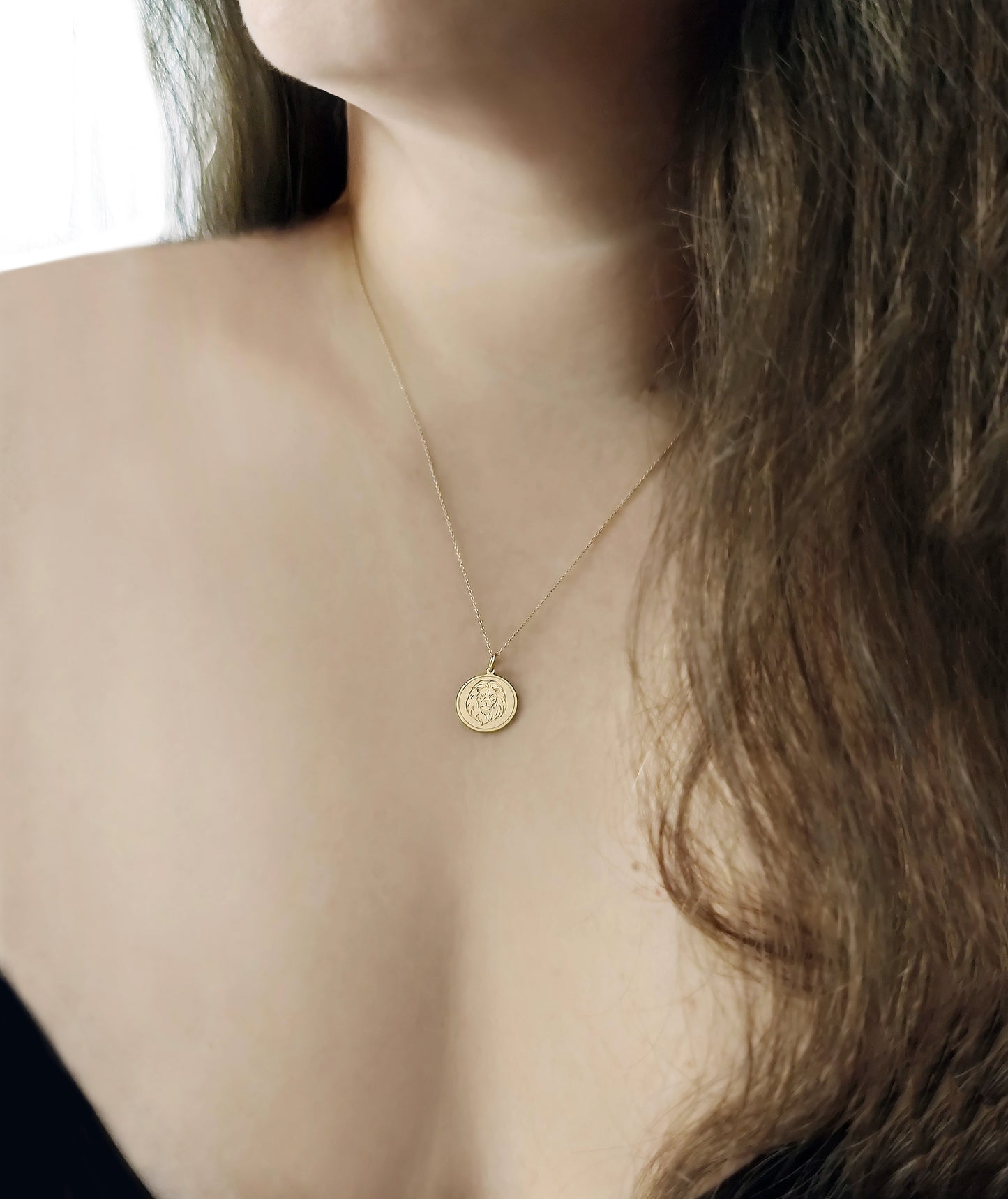 woman wearing yellow gold disc pendant necklace engraved with a lion head and a circle frame around it