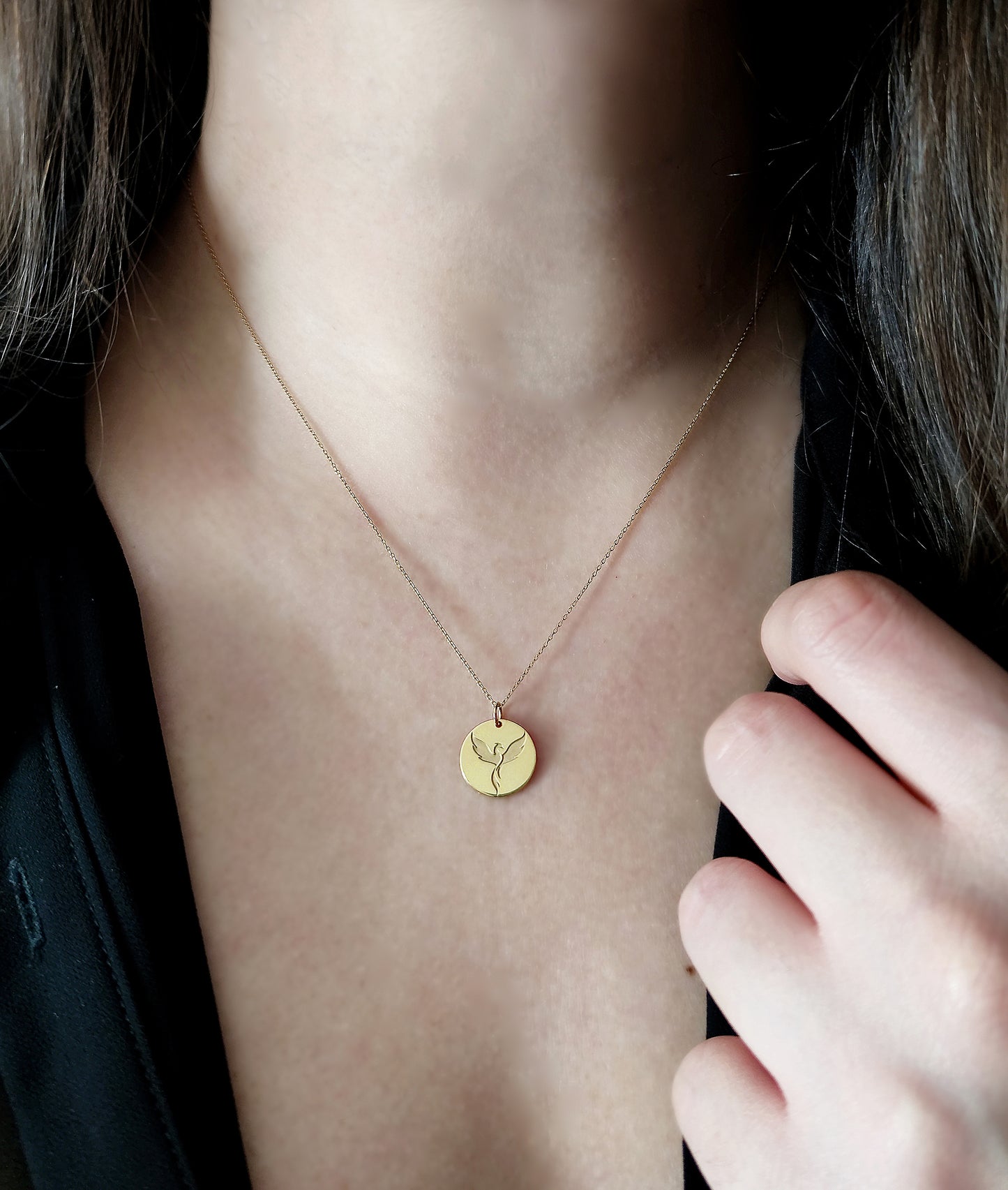 Woman wearing a necklace with a disc pendant engraved with a phoenix firebird