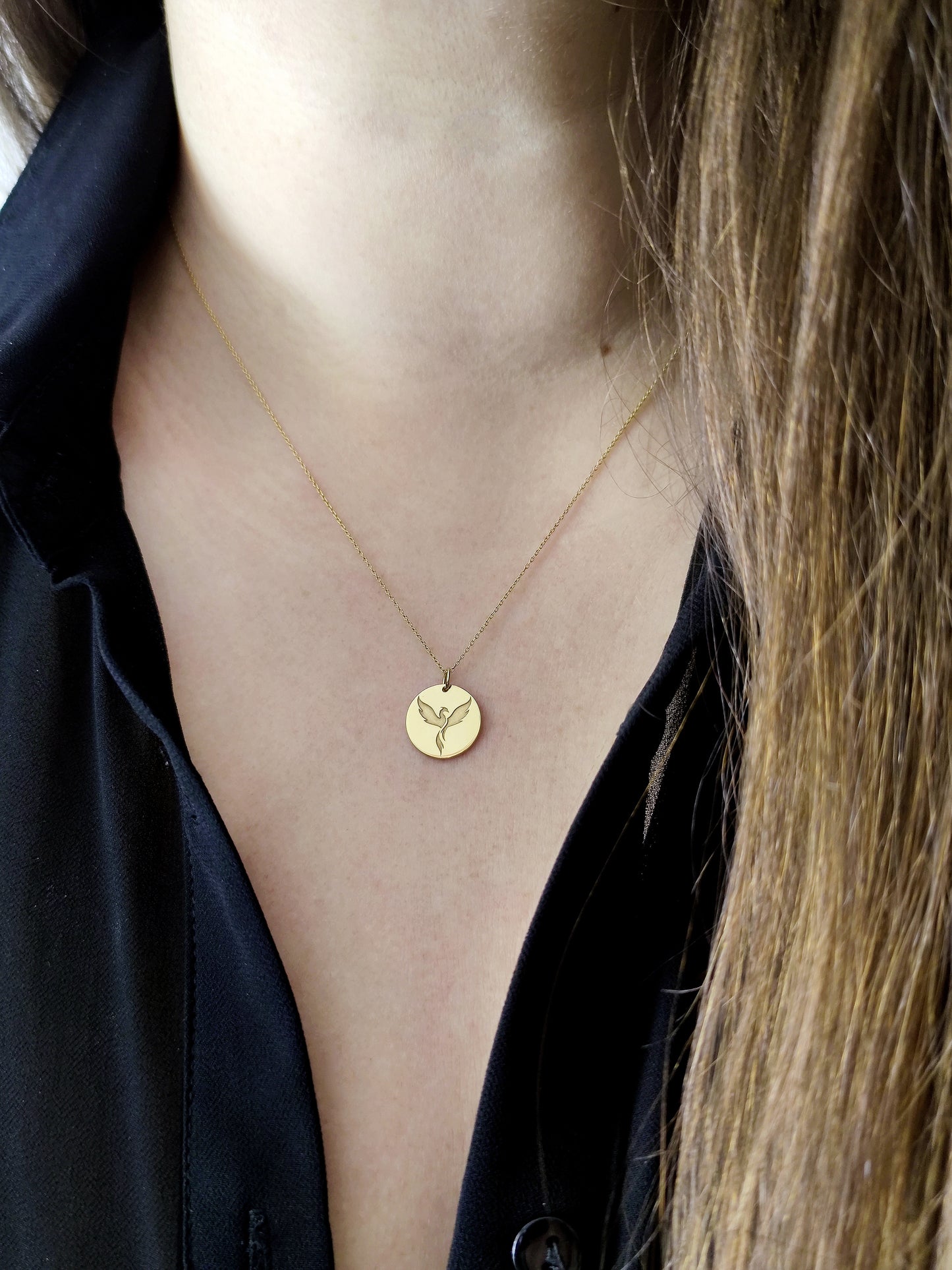 Close up of a woman's neck wearing a necklace with a disc pendant engraved with a phoenix firebird