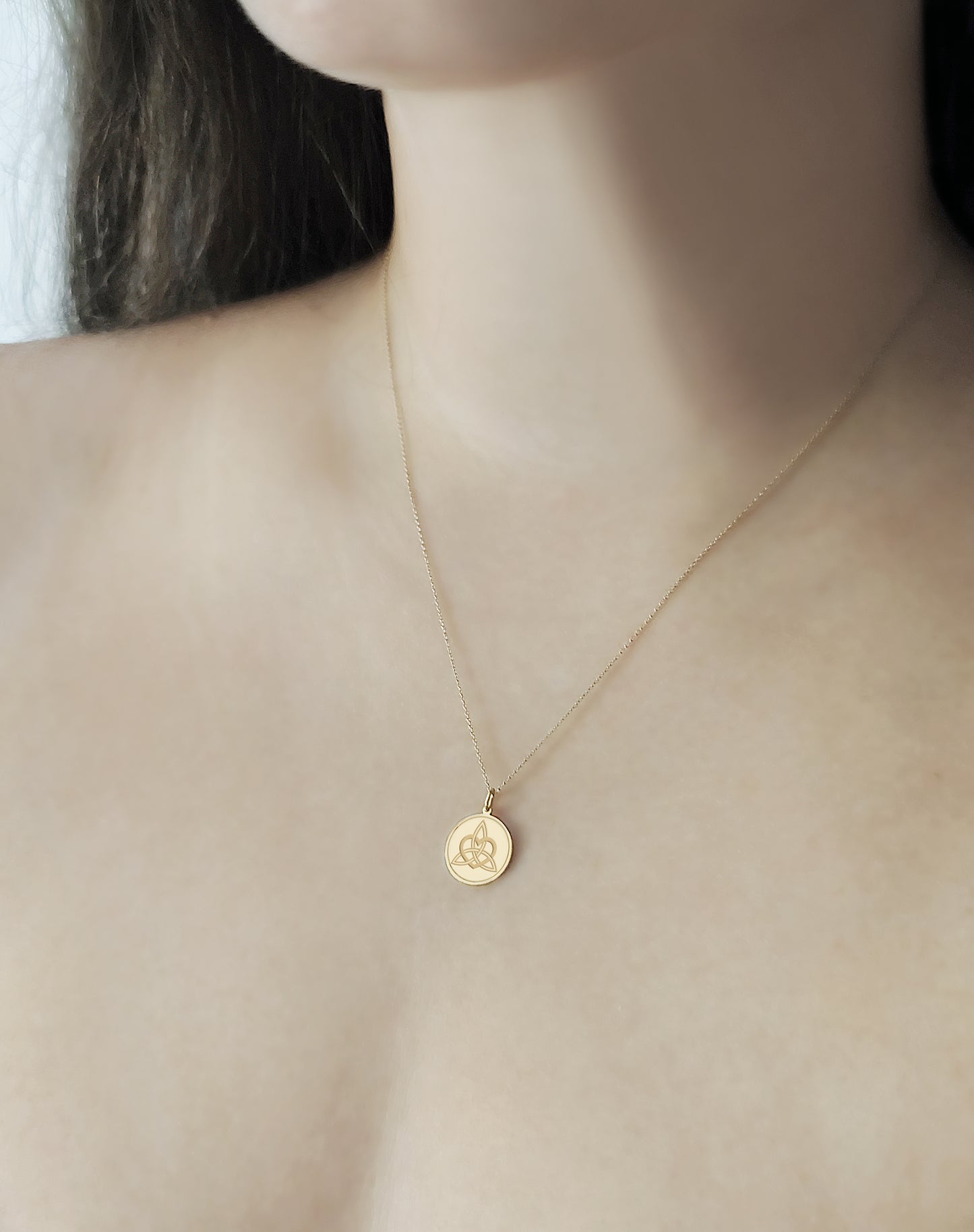 woman wearing gold disc pendant necklace engraved with a triquetra everlasting love celtic knot with a circle frame around it