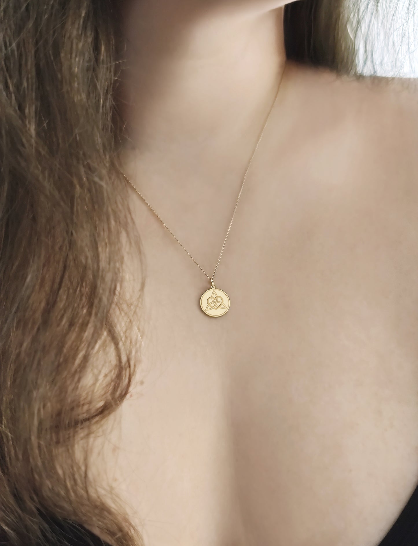 female wearing gold disc pendant necklace engraved with a triquetra everlasting love celtic knot with a circle frame around it