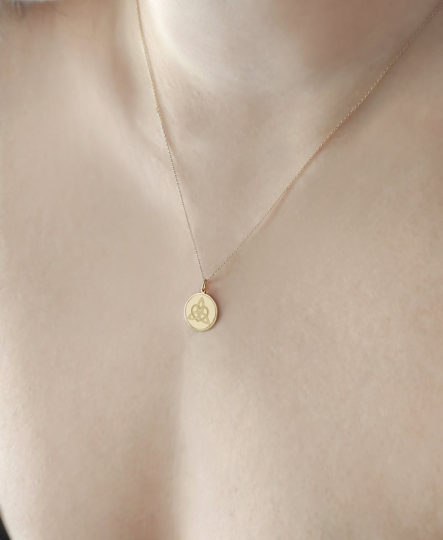 close up of a woman's neck wearing gold disc pendant necklace engraved with a triquetra everlasting love celtic knot with a circle frame around it