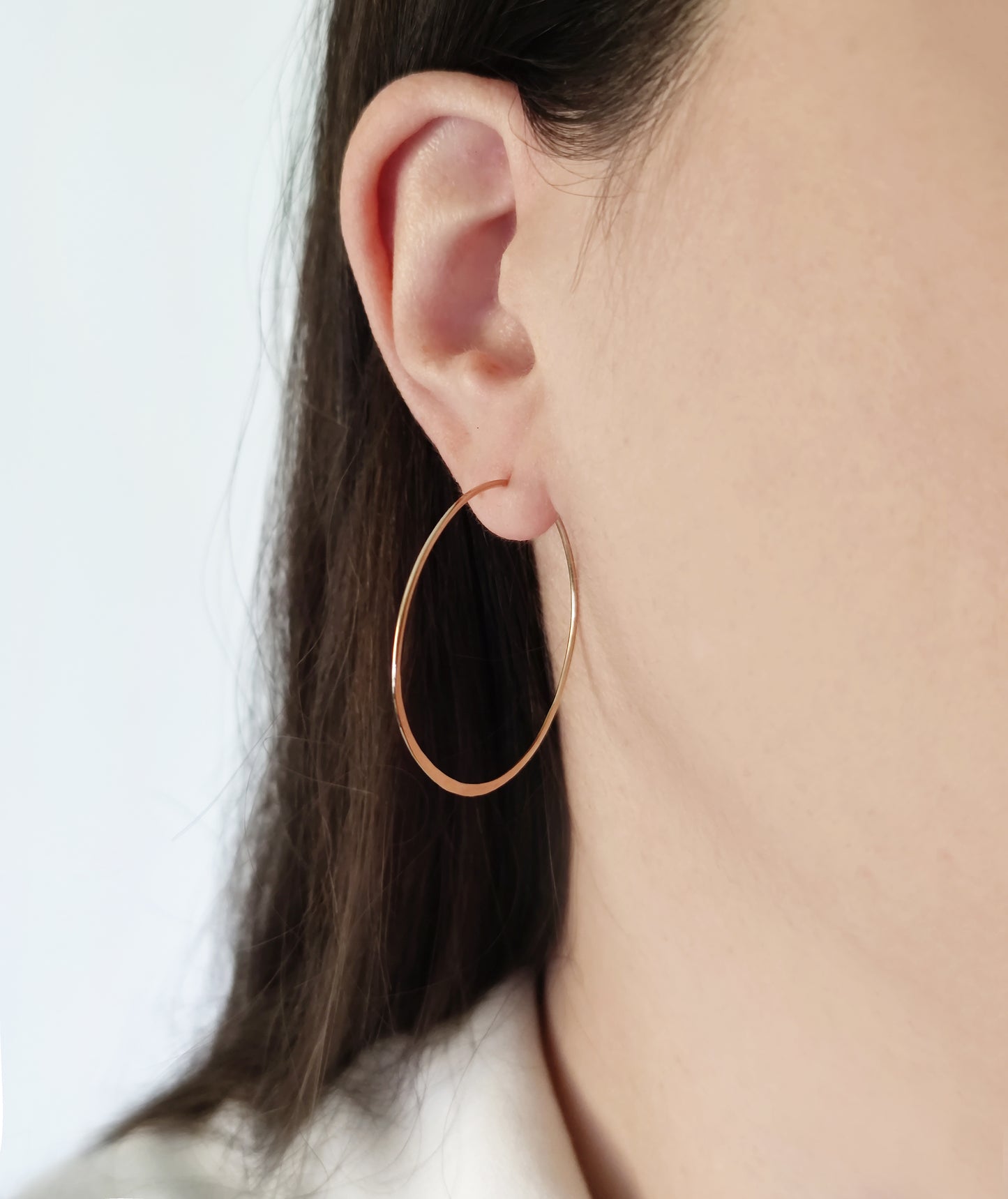 close up a woman's ear wearing yellow gold large thin hoop earring with flattened bottom