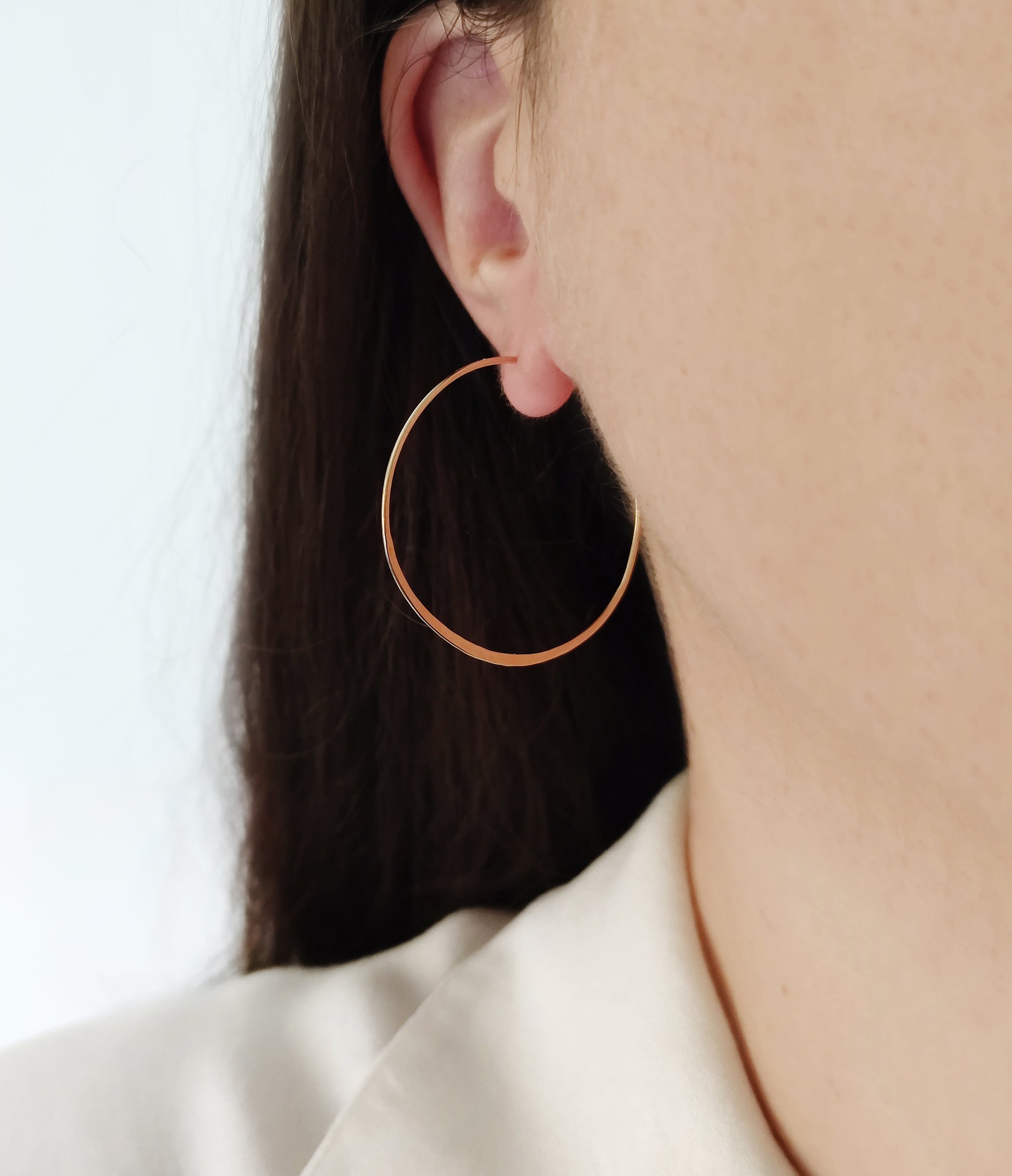 close up a woman wearing yellow gold large thin hoop earring with flattened bottom