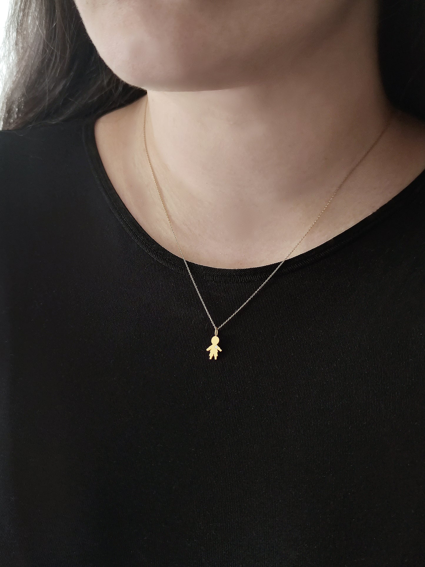 close up of a woman's neck wearing a gold necklace with a tiny boy charm set with a tiny diamond