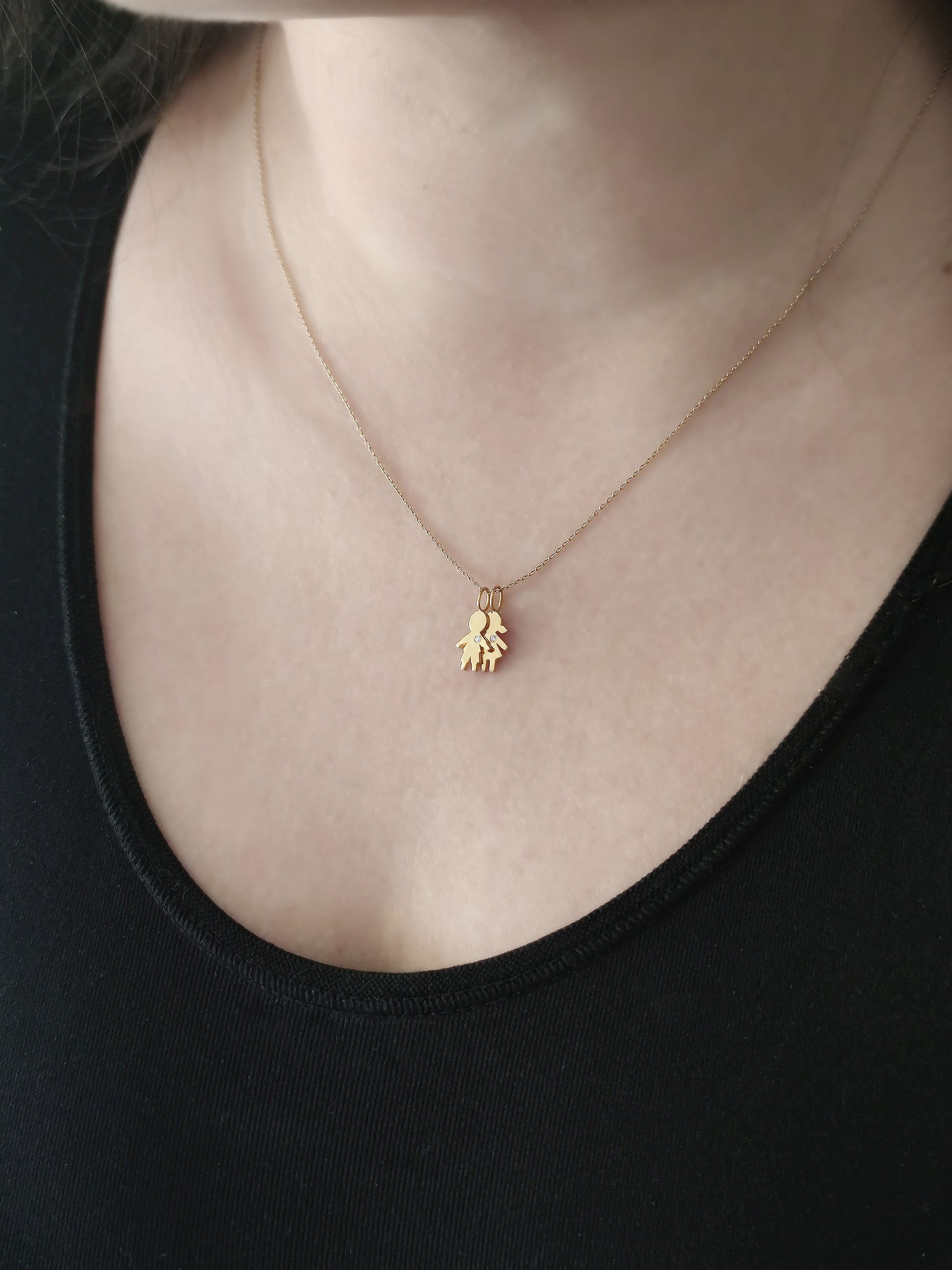 close up of a woman's neck wearing a gold necklace with a tiny boy and a tiny girl charm set with tiny diamond