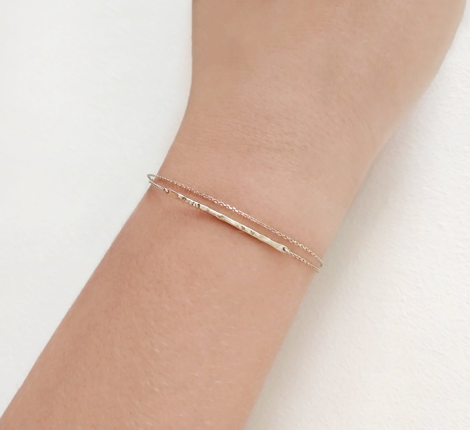 female wrist wearing solid yellow gold bracelet with a thin hammered bar and double thin chain