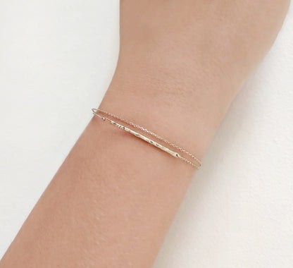 female wrist wearing solid yellow gold bracelet with a thin hammered bar and double thin chain