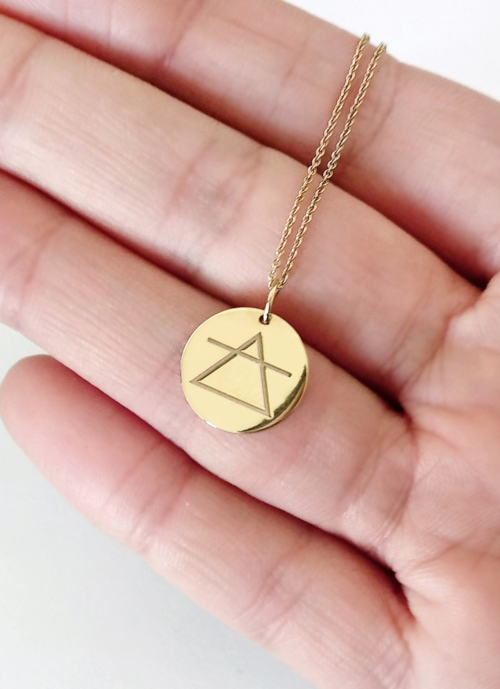 hand holding yellow gold necklace with a disc pendant engraved with the air element for size reference