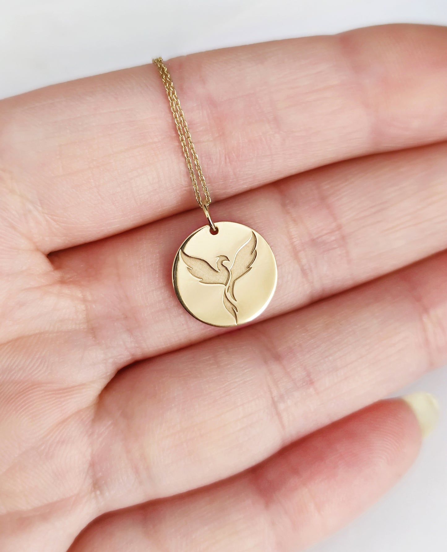 Palm of a woman holding a gold phoenix pendant necklace for size reference
