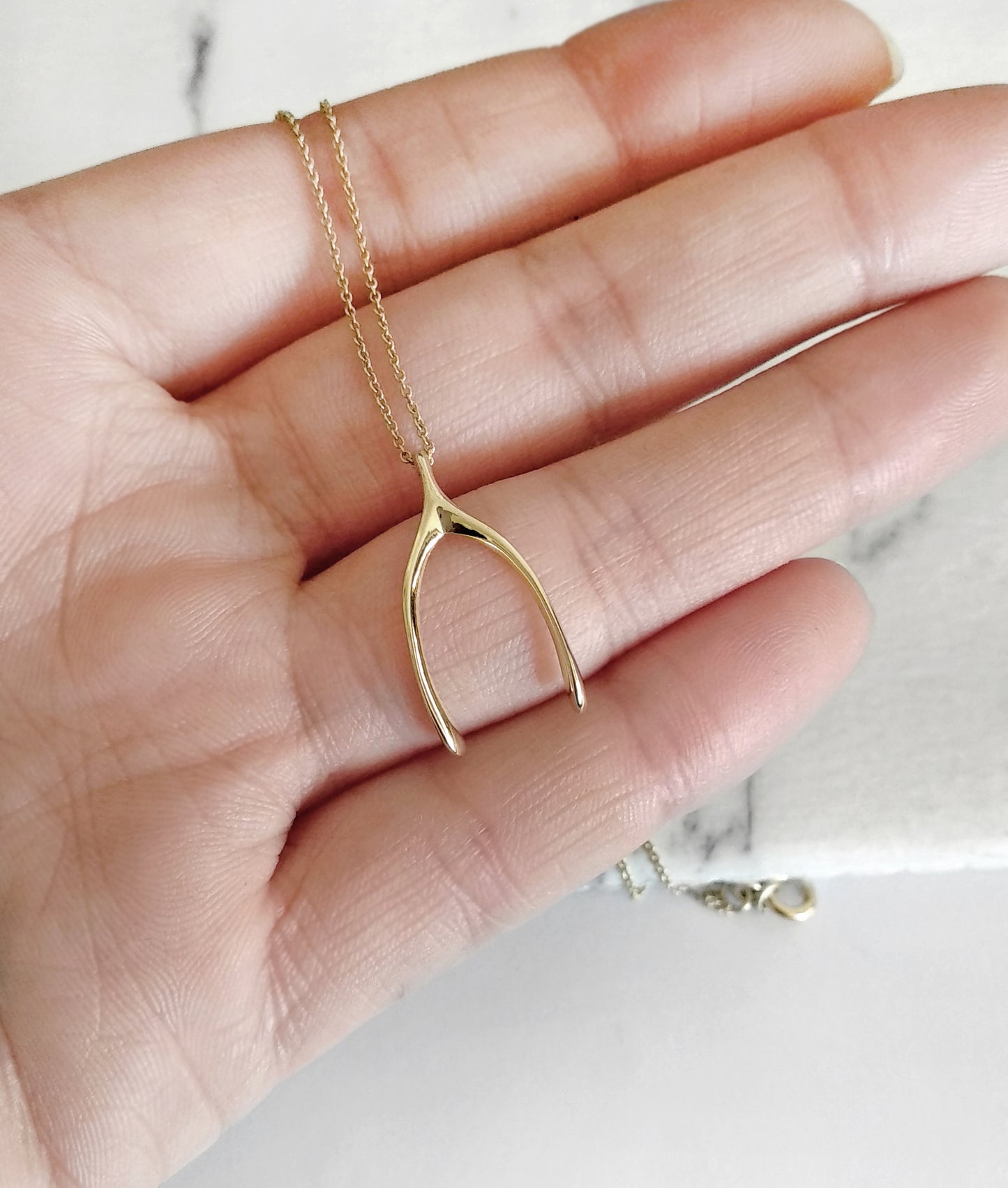 hand holding solid yellow gold wishbone pendant necklace for size reference