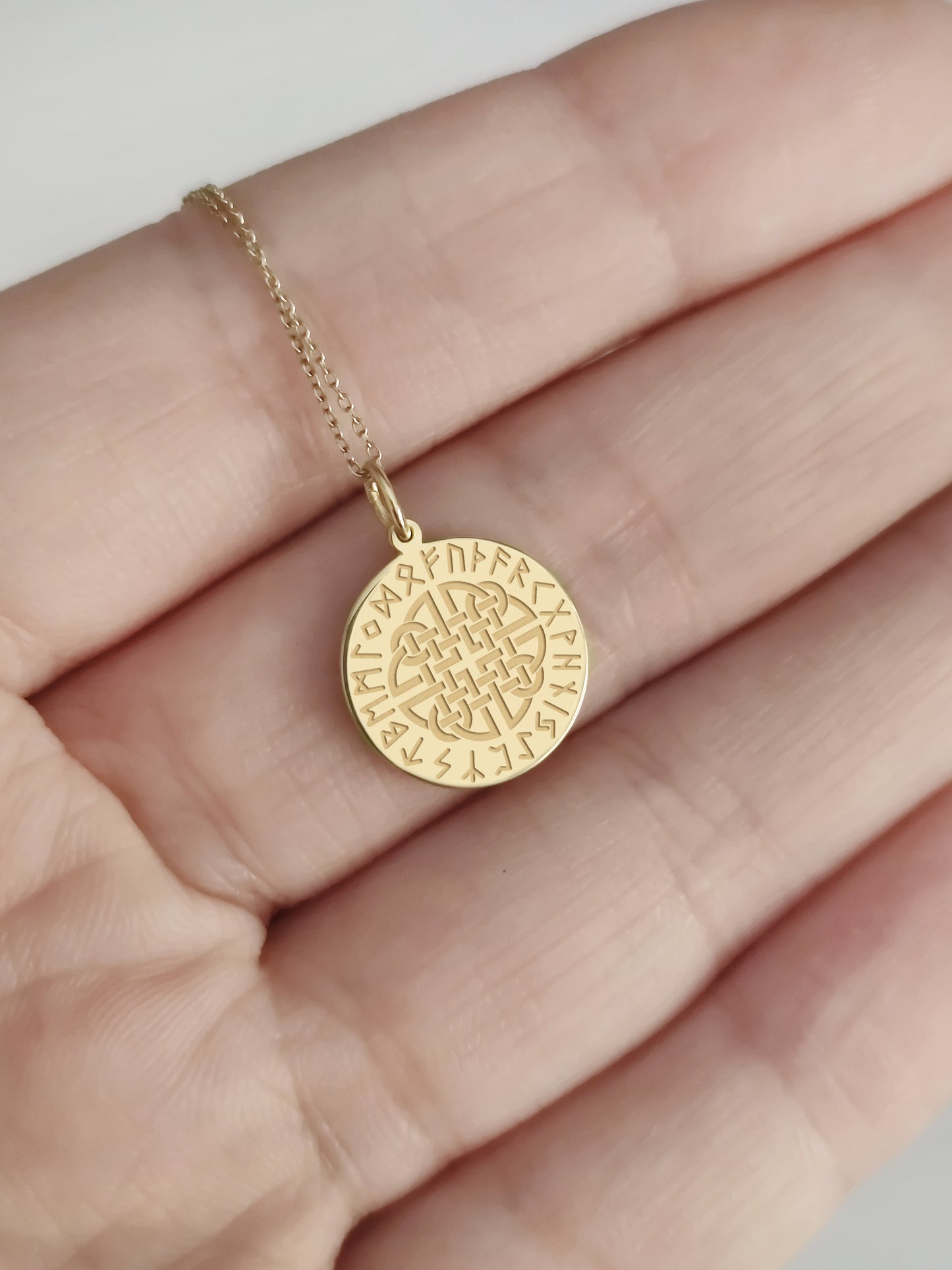 hand holding gold pendant with engraved dara knot and runes for size reference