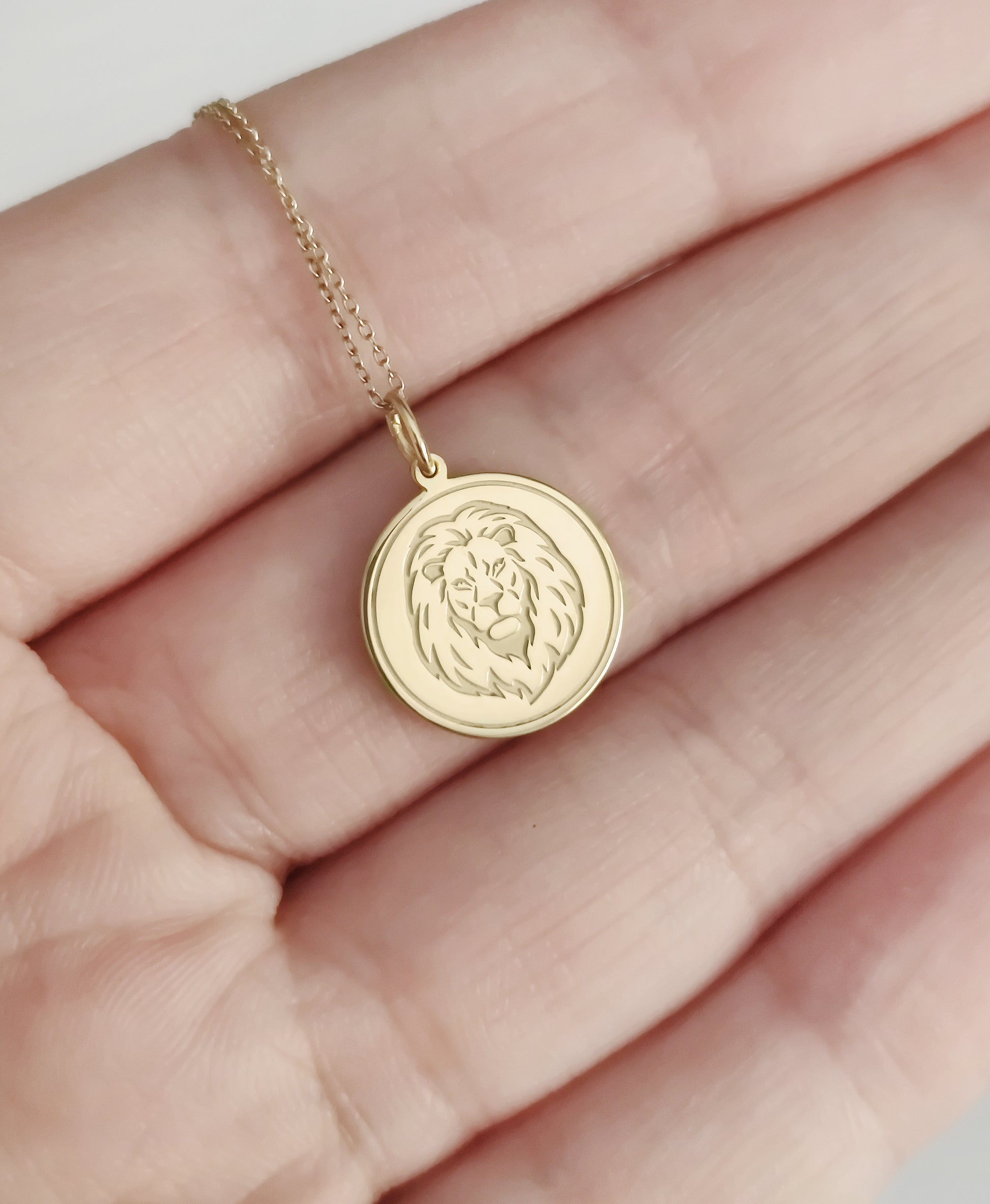 hand holding for size reference a yellow gold disc pendant necklace engraved with a lion head and a circle frame around it