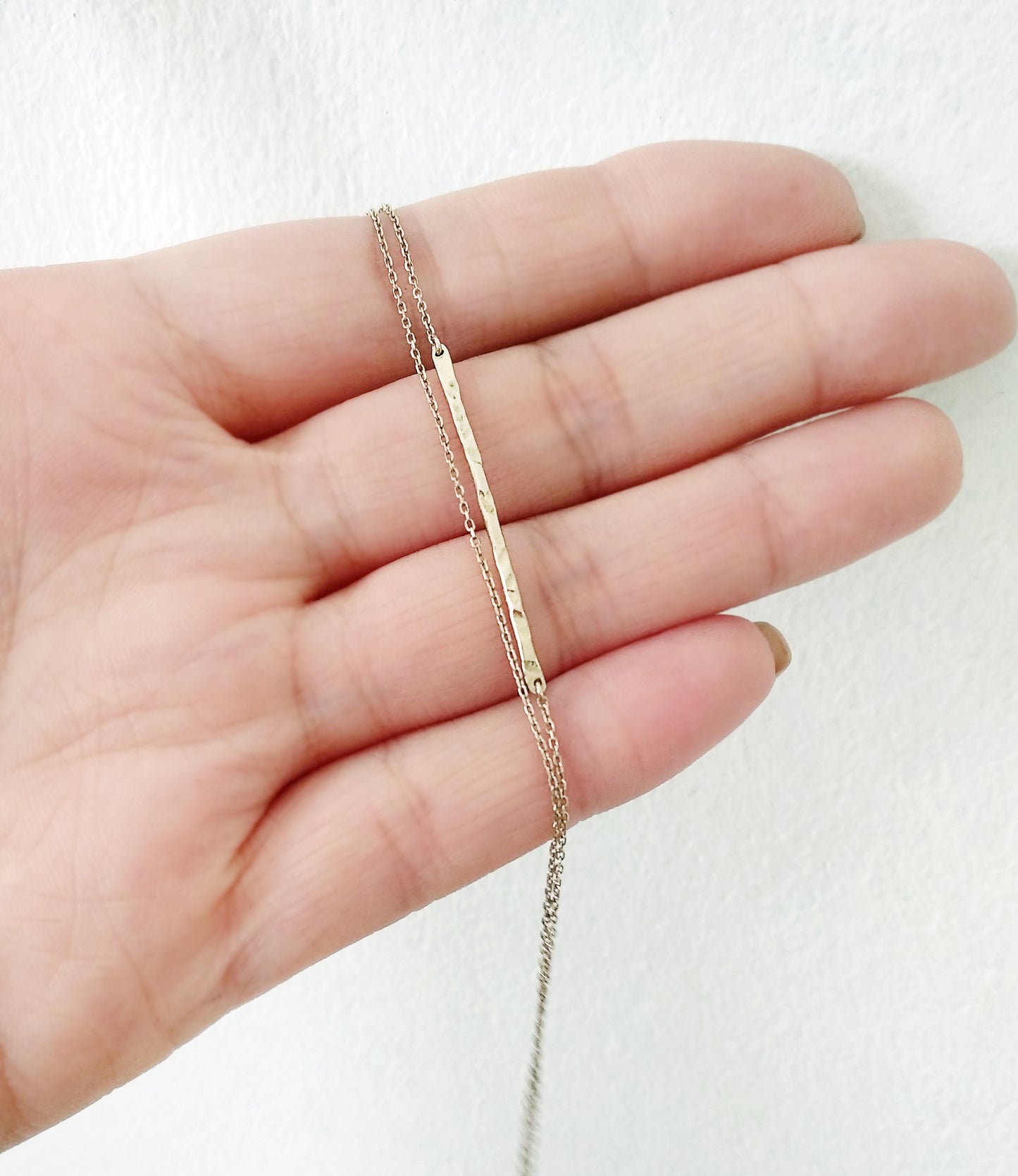 hand holding a solid yellow gold bracelet with a thin hammered bar and double thin chain