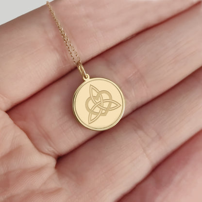 hand holding gold disc pendant necklace engraved with a triquetra everlasting love celtic knot with a circle frame around it