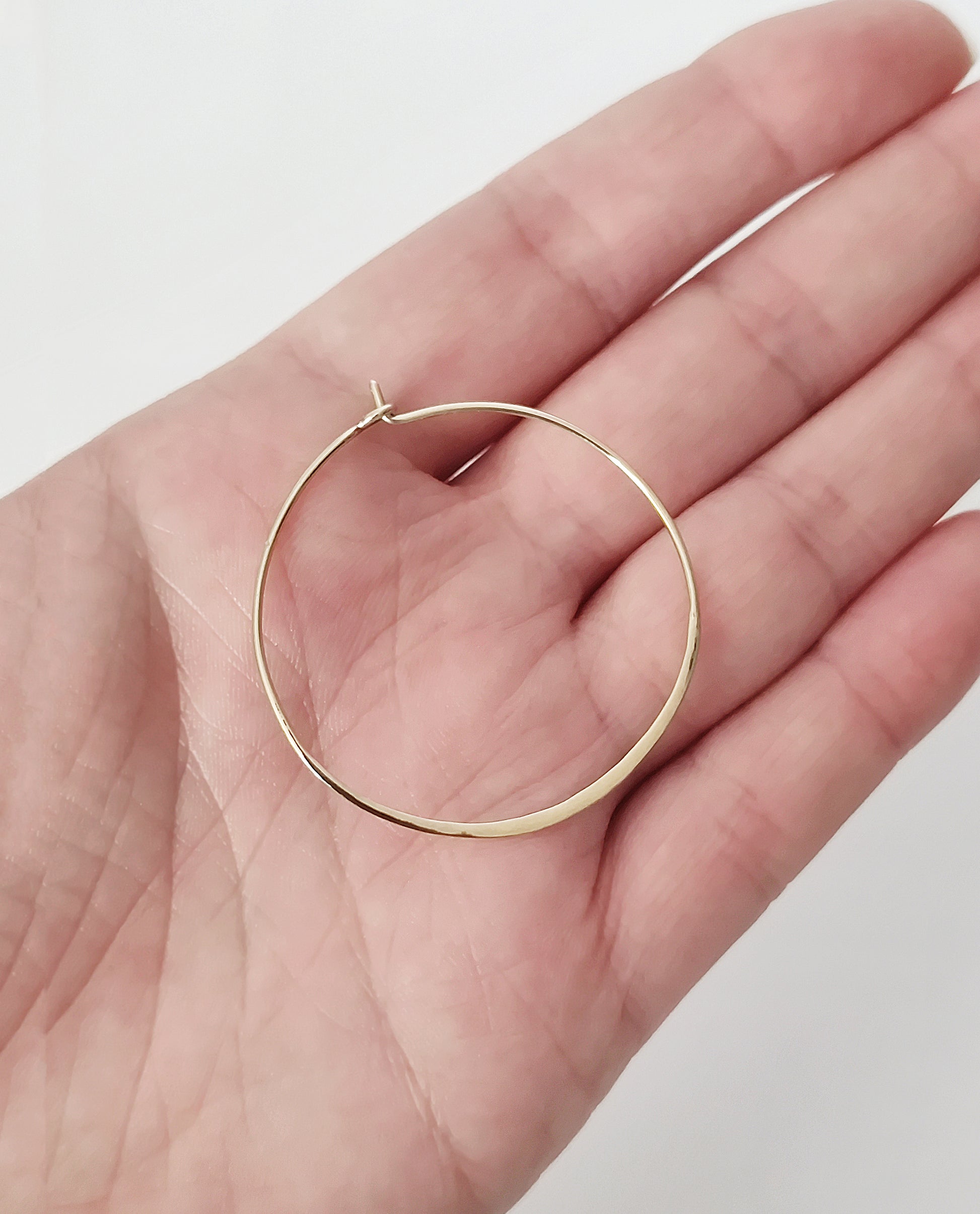 close up of a palm holding a yellow gold hoop earring for size reference