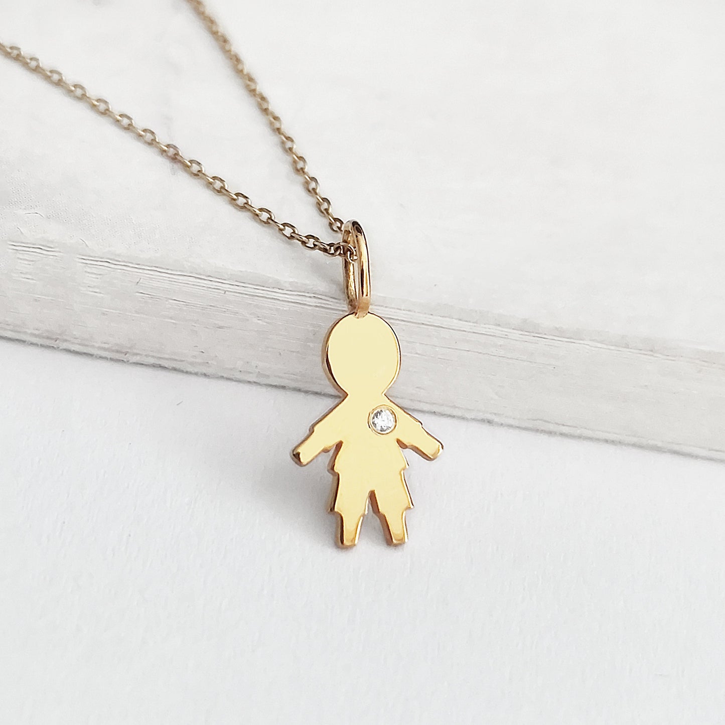 close up of a yellow gold necklace with tiny boy outline charm set with tiny diamond