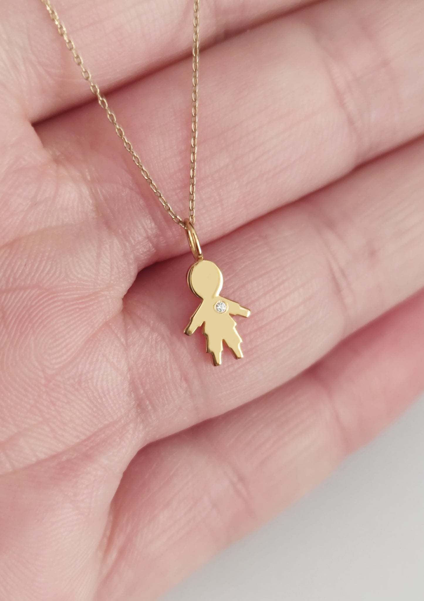 close up of a palm holding a gold necklace with a tiny boy outline charm set with a diamond 