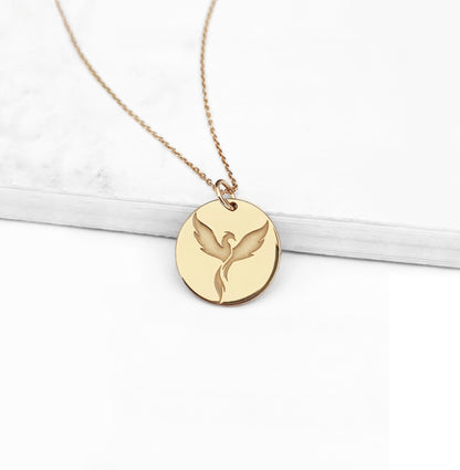 close up of a yellow gold pendant necklace engraved with a phoenix firebird